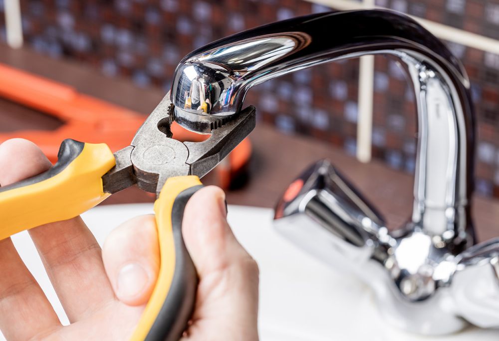 A person fixes a faucet using pliers. 