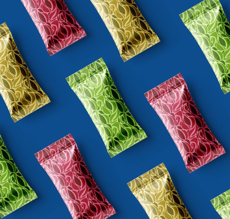 Colorful foil flexible snack pouches with leaf pattern green gold red arranged diagonally on blue background. 