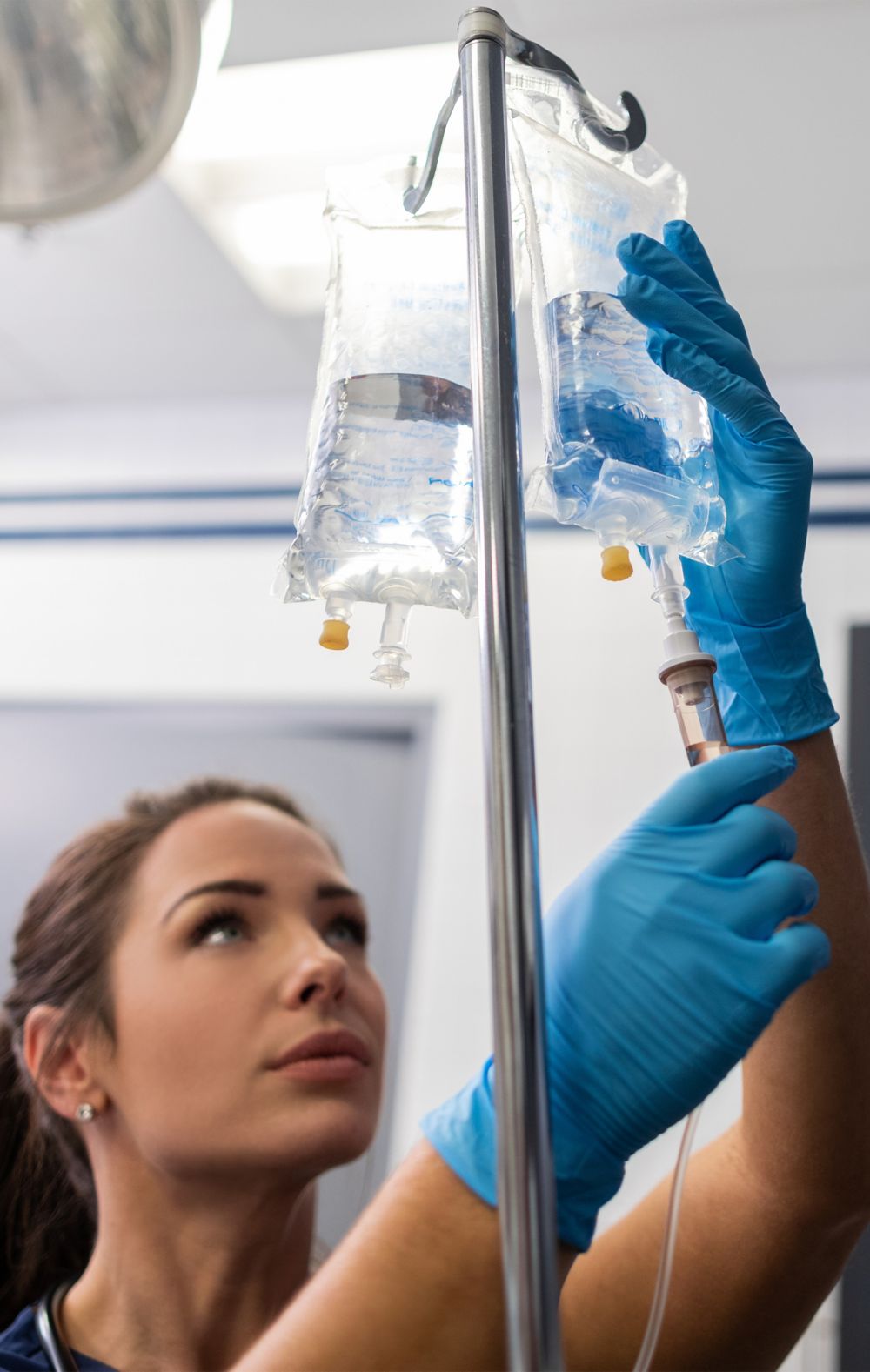 A medical professional hangs a IV bag with clear fluid. 