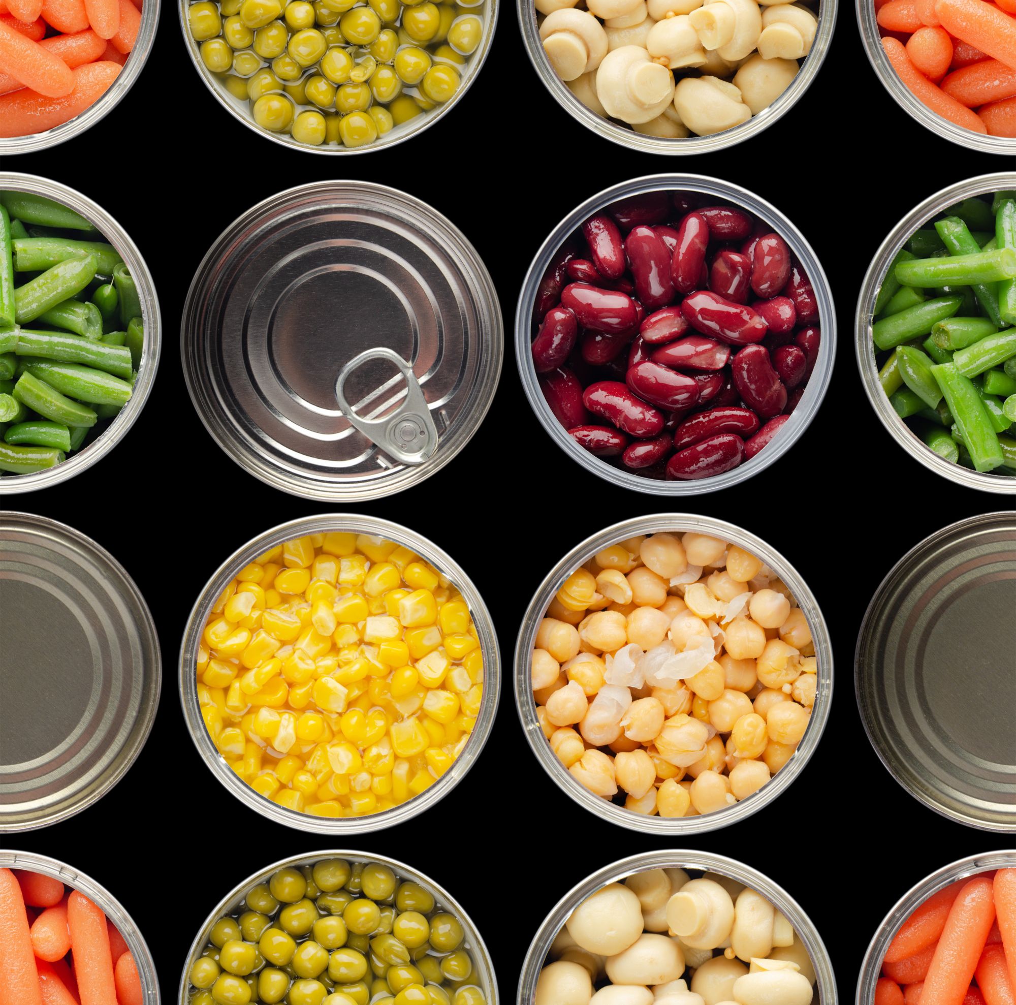 Flat lay view of canned vegetables including corn, chickpeas, pears, carrots, beans and mushrooms. 