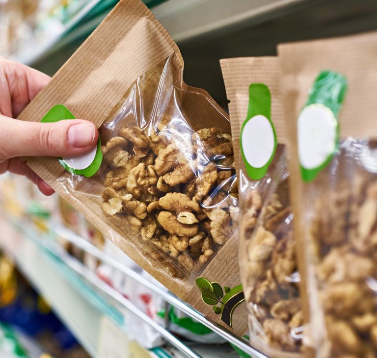 A package of granola is pulled from a grocery shelf. 