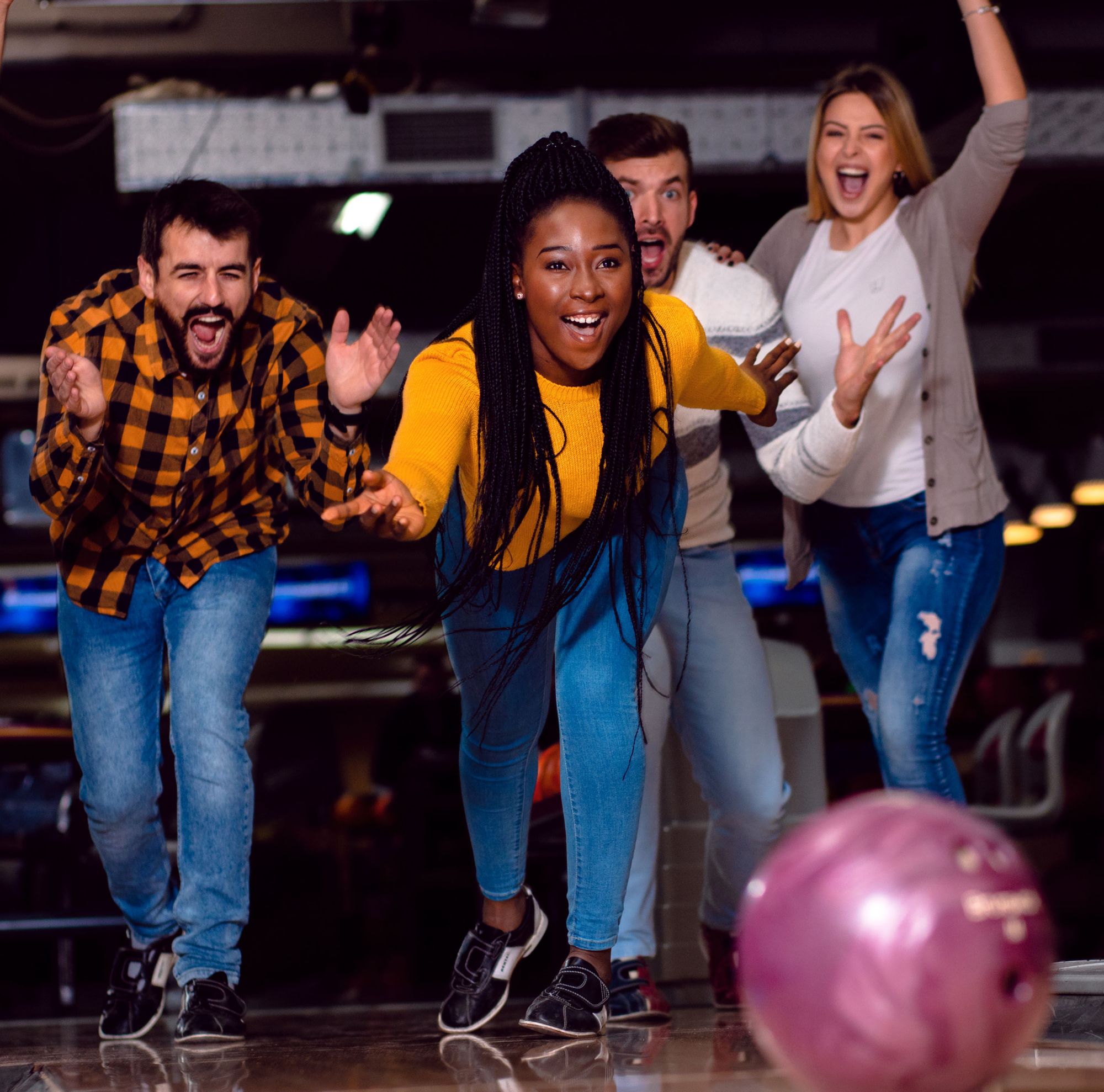 Four people cheer while watching a bowling ball roll. 