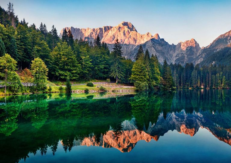 Summer morning landscape of Fucine Lake in Italy with the mountain range reflecting on the water’s surface.  