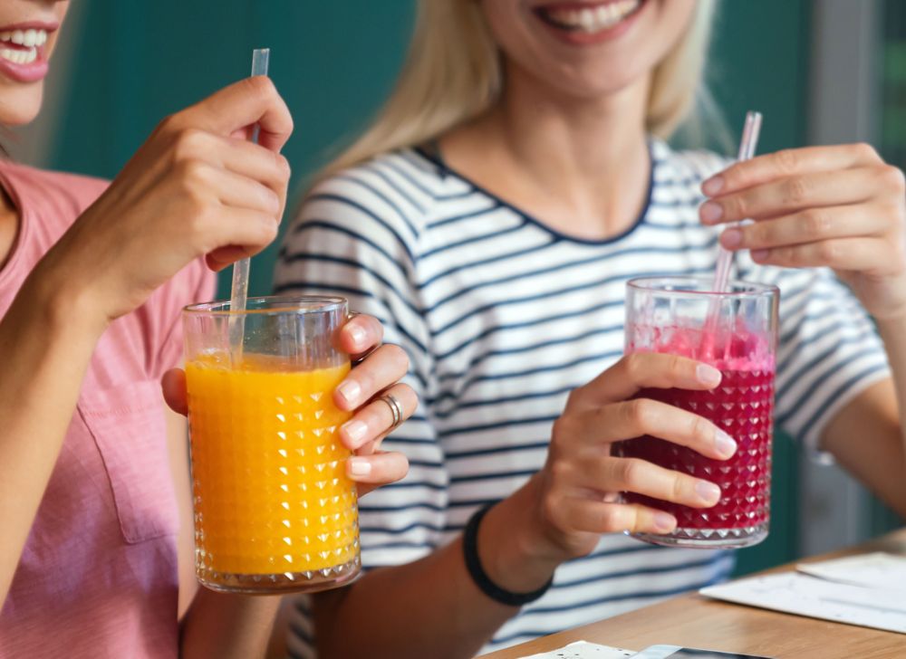 Two people hold drinks in one hand and the drink’s straw in the other hand 
