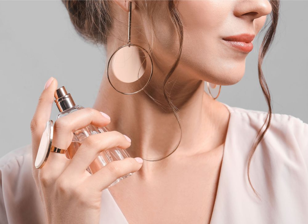 Close-up of a clear bottle of perfume being sprayed on a person’s neck.   