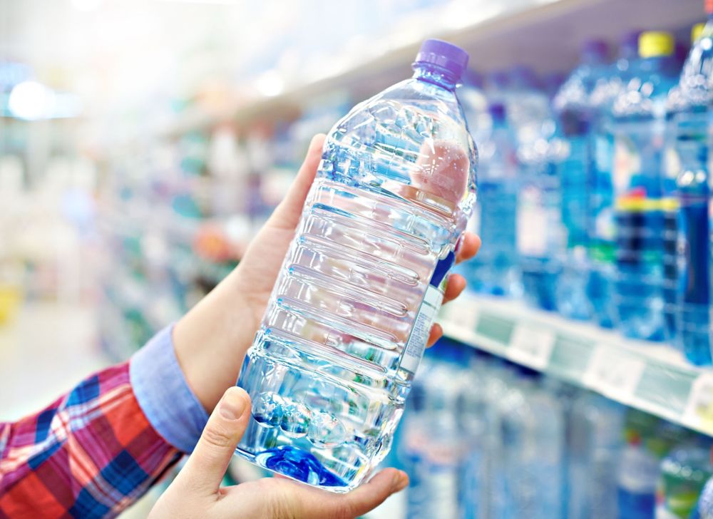 Hand holding water bottle in supermarket aisle. 