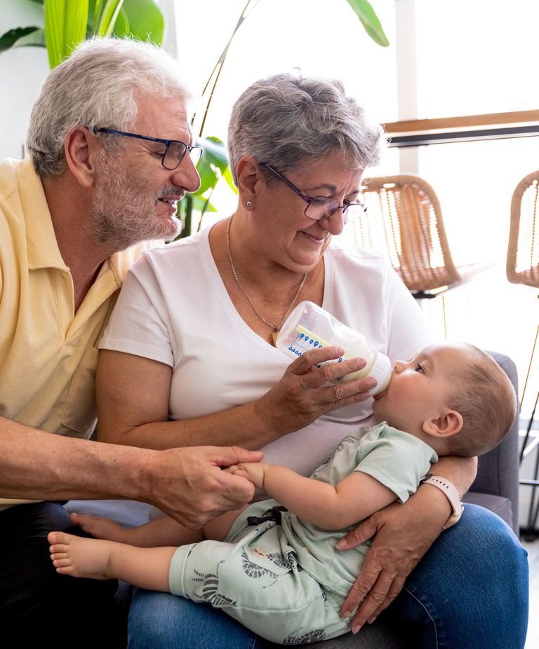 Grandparents feeding a baby with a clear baby bottle full of milk. 
