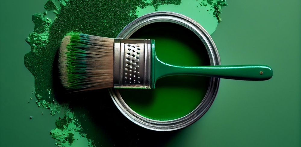 A paintbrush sits atop a can of green paint, which sits on a freshly painted green surface. 