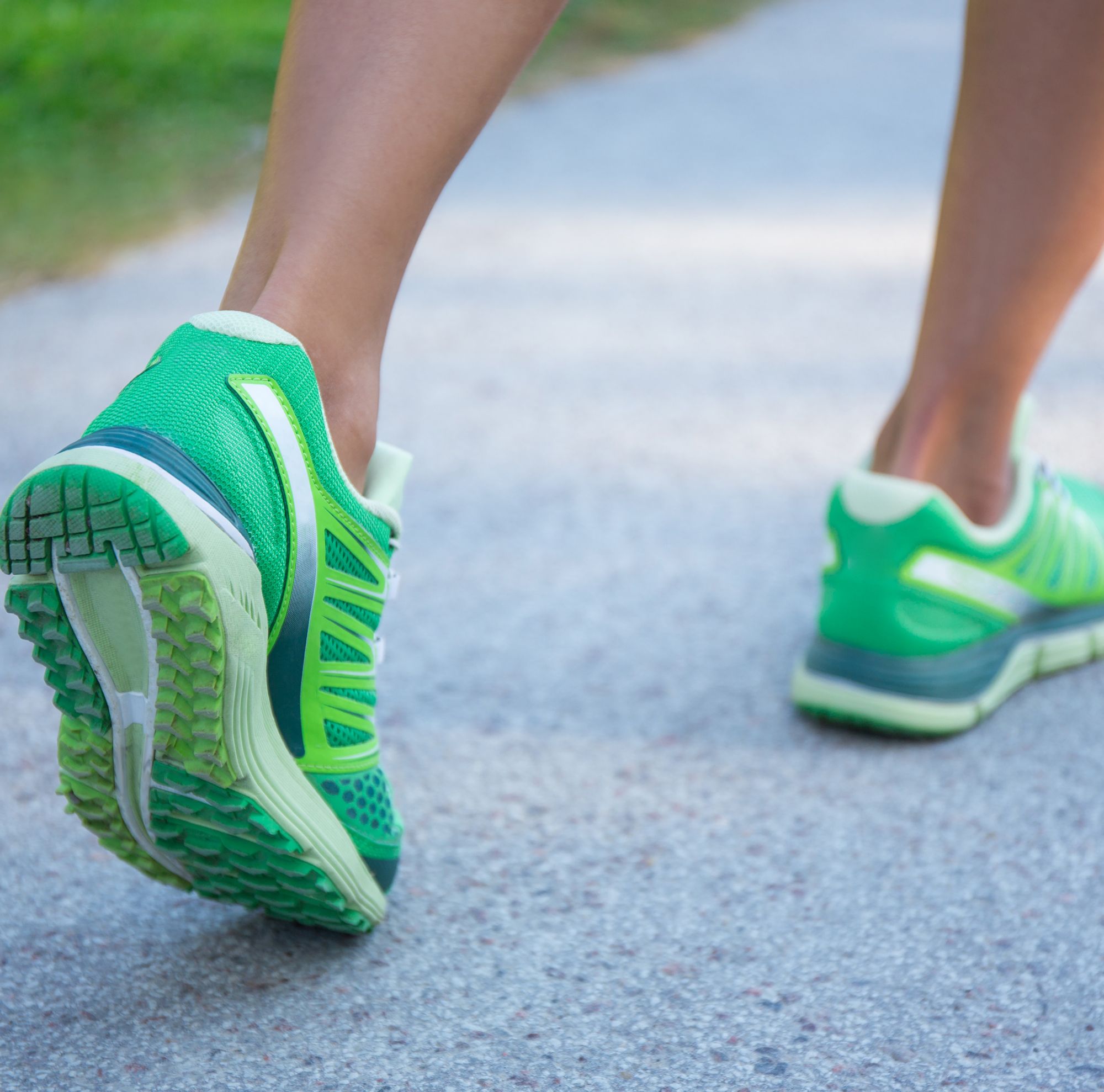 A runners legs in green shoes swiftly running on an asphalt road 