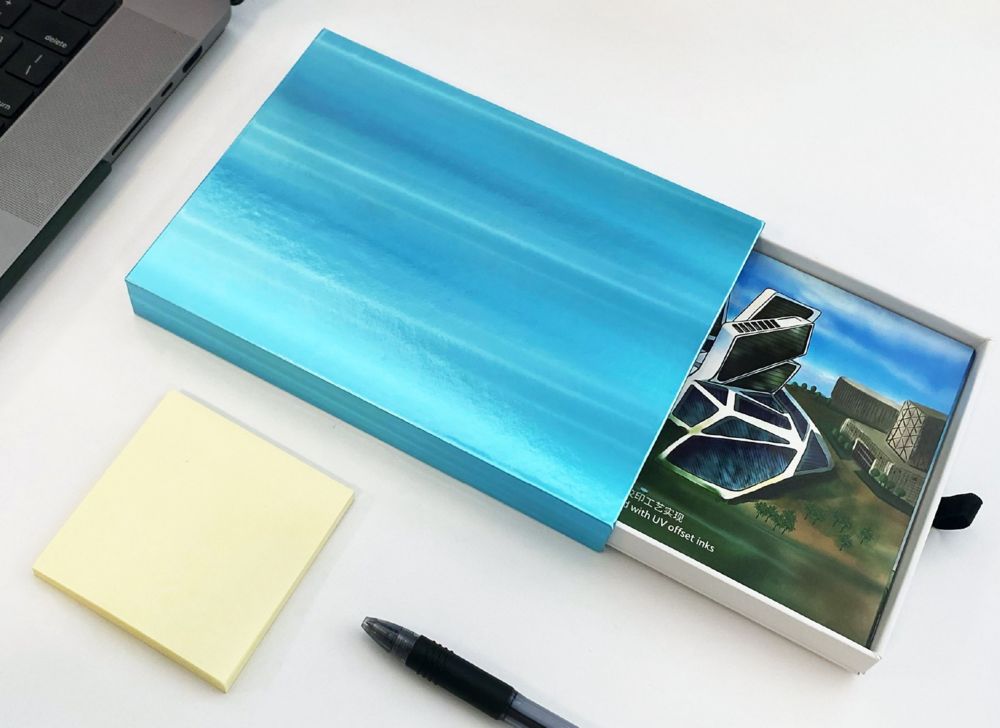 A bright blue business card holder lies partially open on a white surface with sticky notes and a laptop next to it. 
