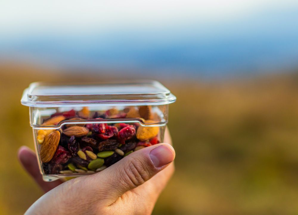 A person holds up a container of trail mix. 