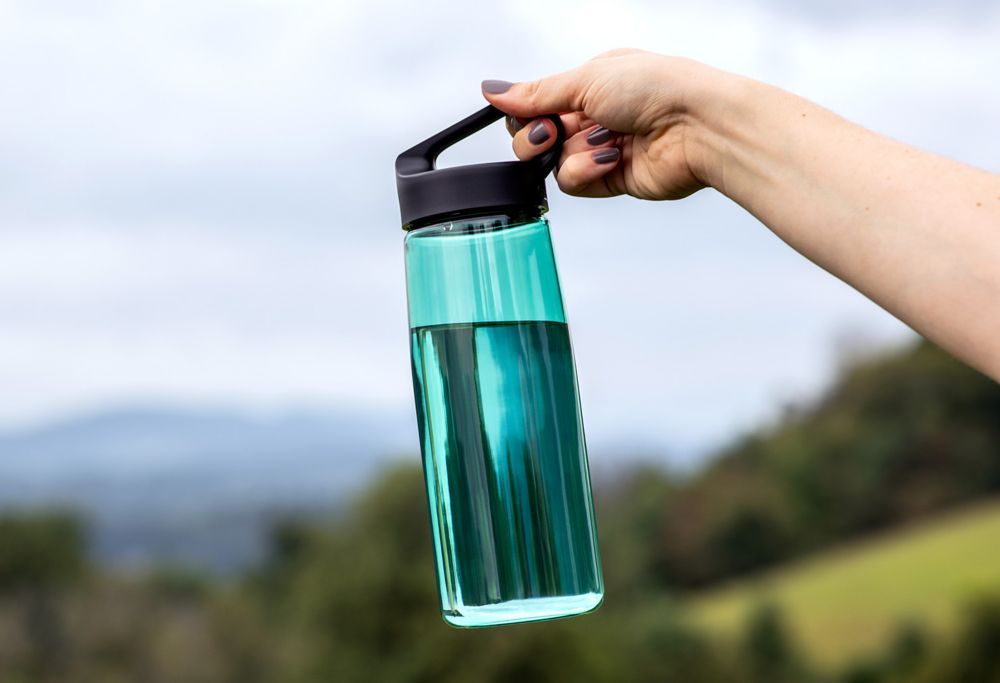 Close-up of person holding a teal reusable water bottle made from Tritan. 