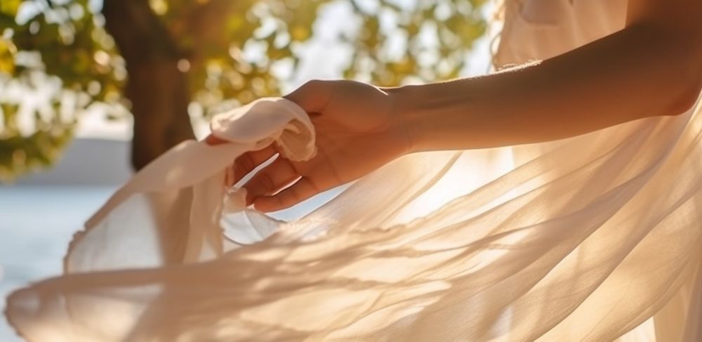 A close up shot of a hand holding the end of a flowy white dress. 