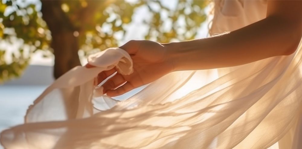 A close up shot of a hand holding the end of a flowy white dress. 