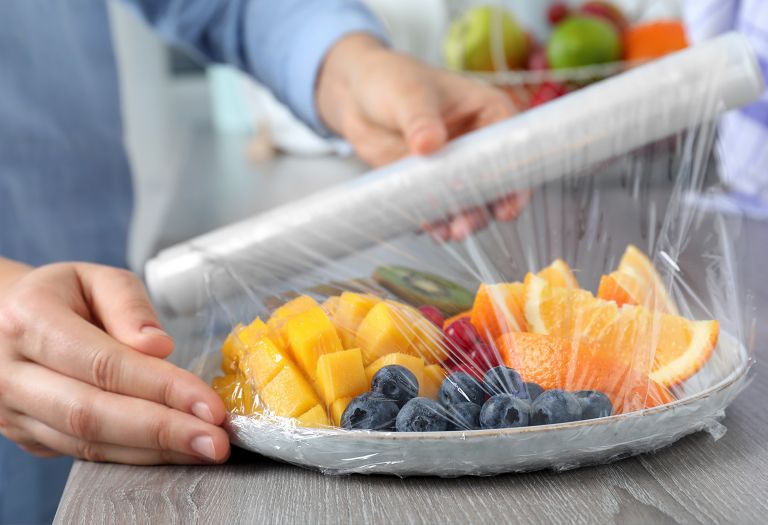 Person covering a fruit plate with food-safe plastic wrap.  