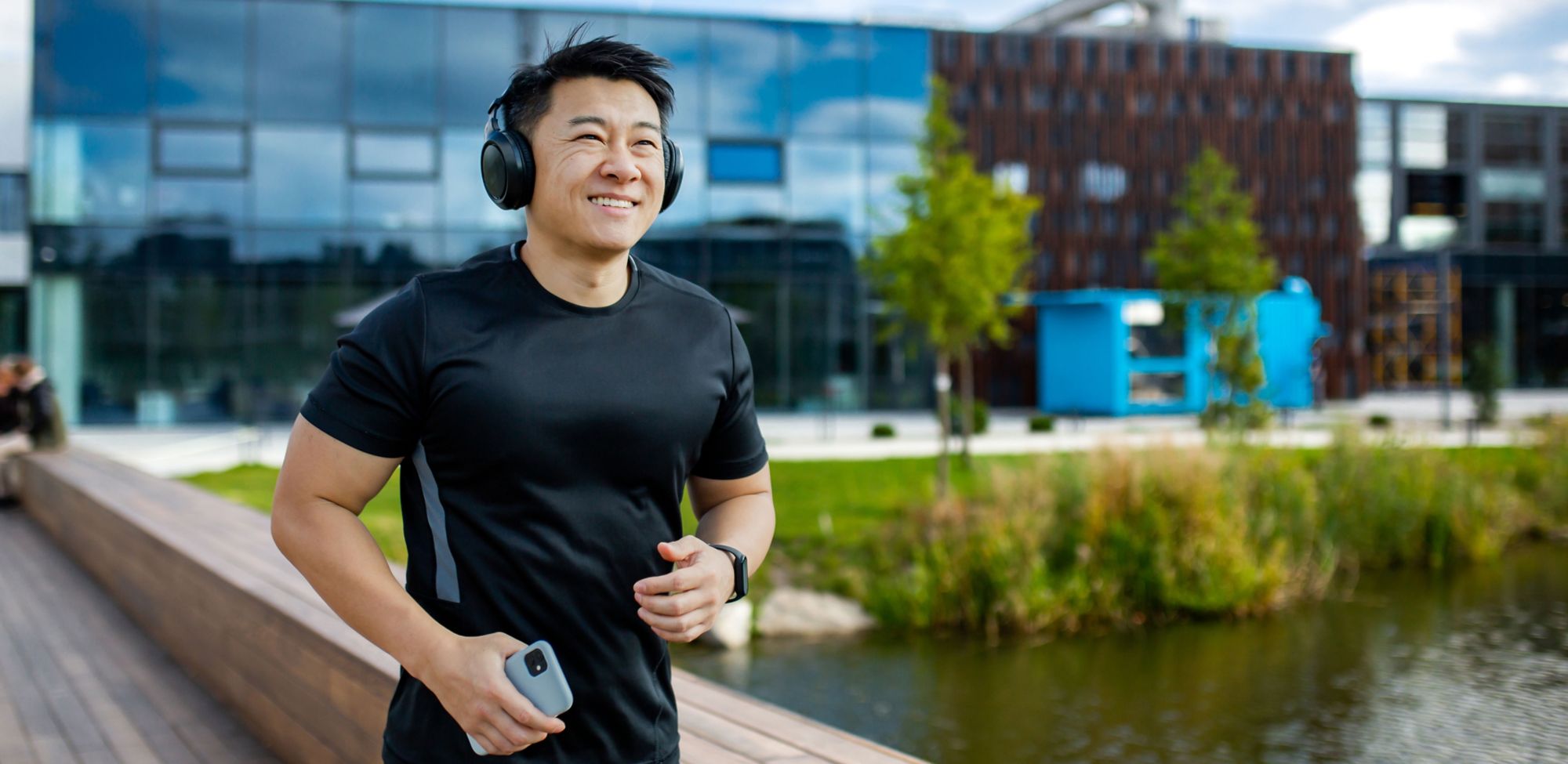 A smiling jogger wearing headphones and carrying a cell phone. 