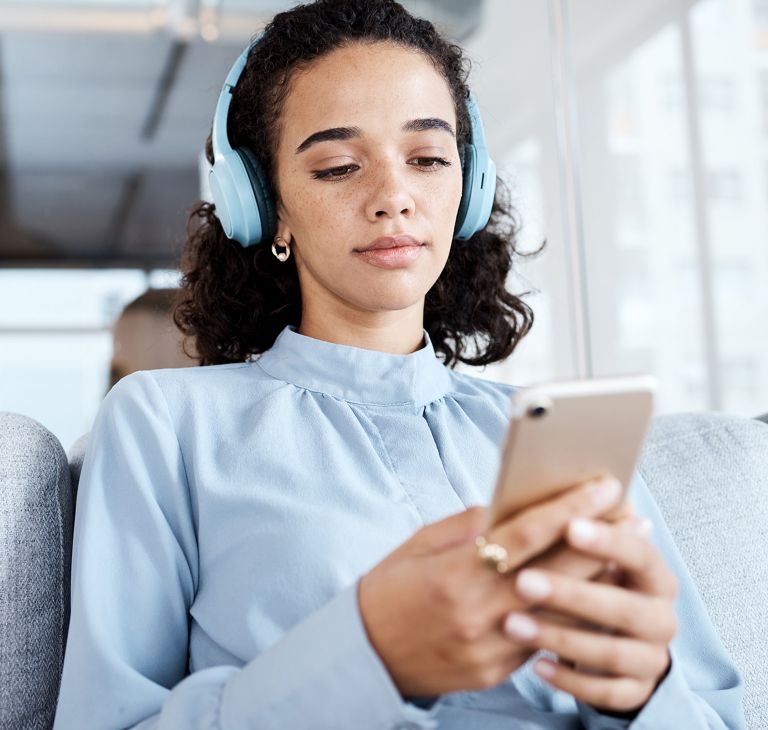 A person wearing over-ear headphones looks at their cell phone. 