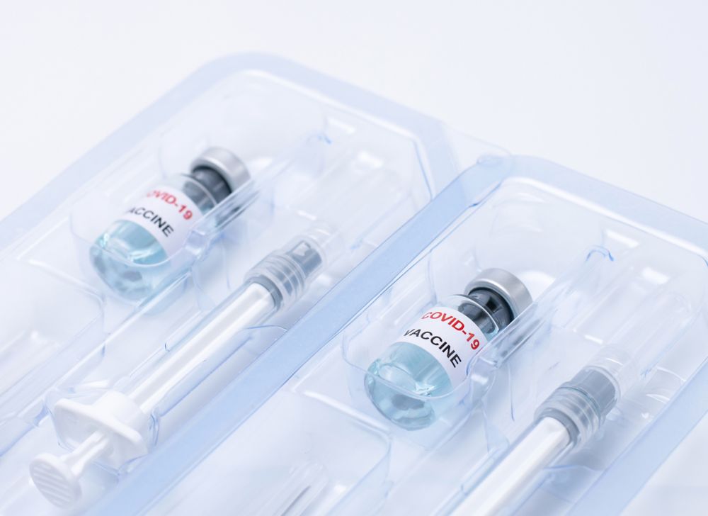 Two sets of plastic packaging each with a syringe and a vaccine-filled glass vial. 