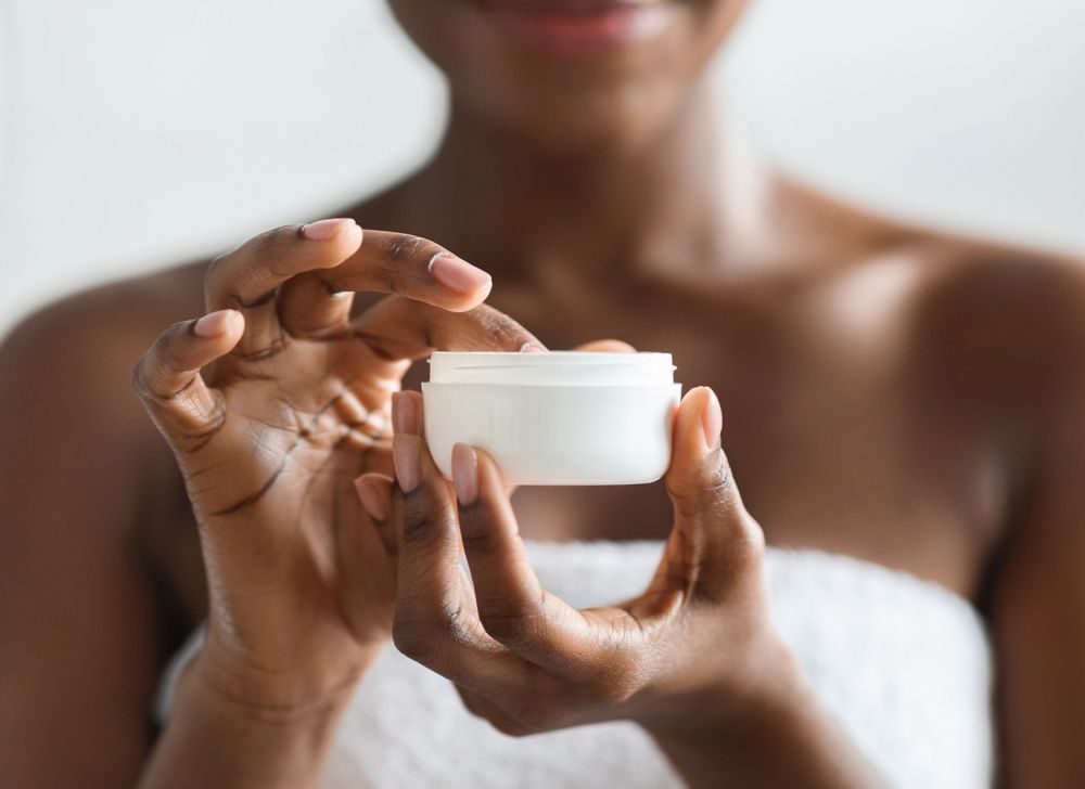 A person holds a jar of skin care cream.  