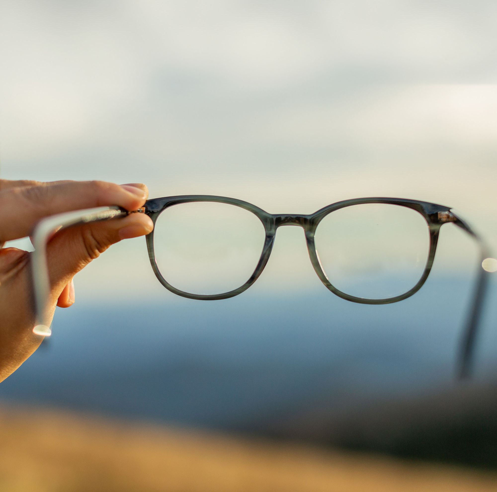 A pair of glasses is held up to a blue sky. 