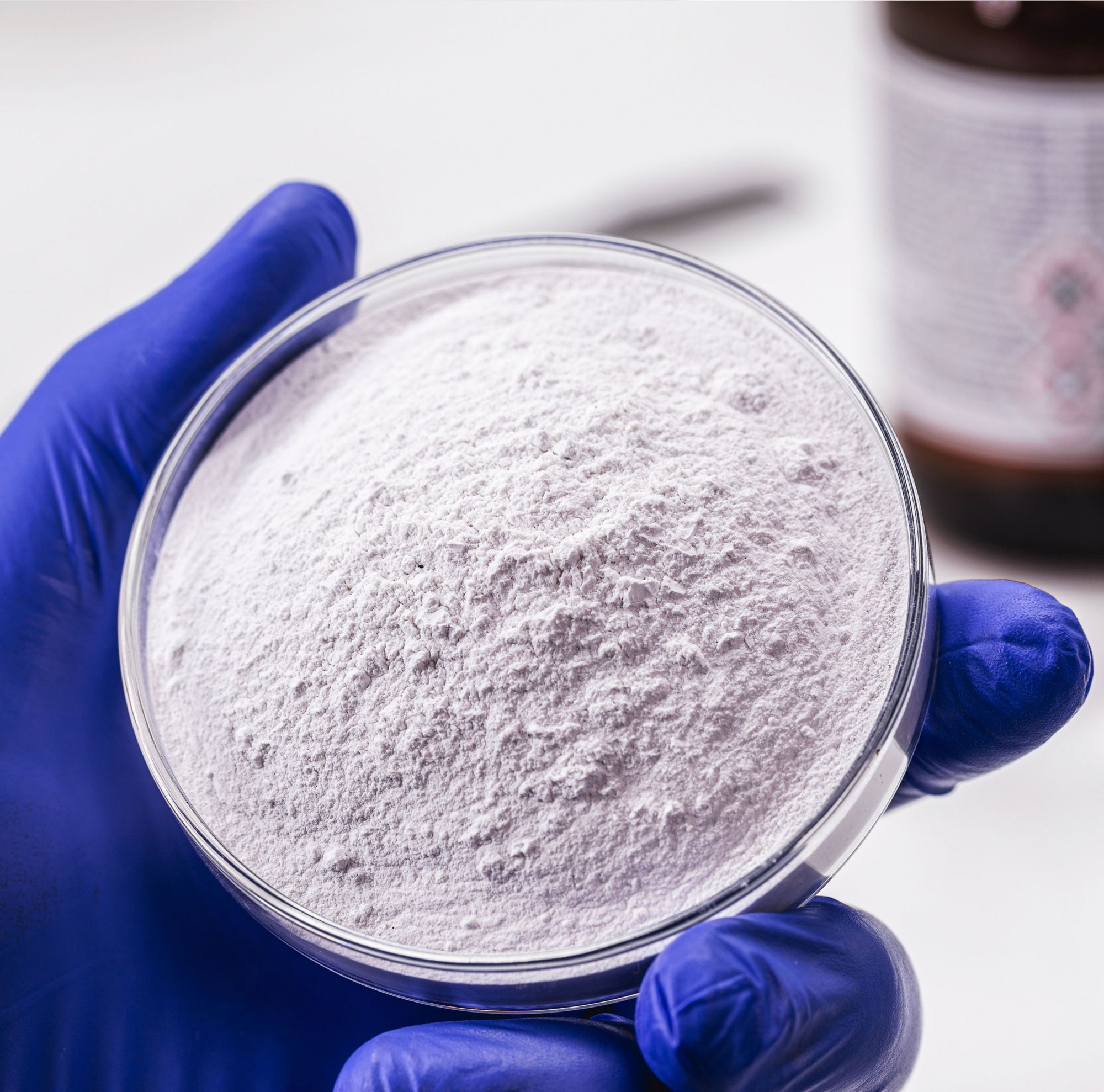 A technician holding a petri dish filled with white powder. 