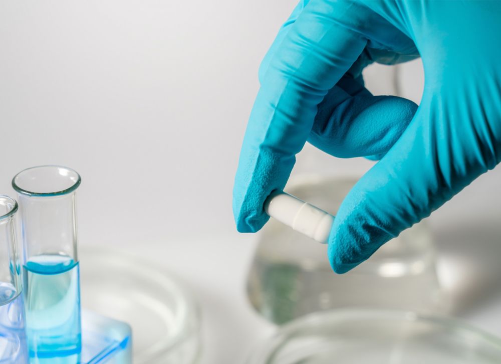 A gloved hand holding a white pill 