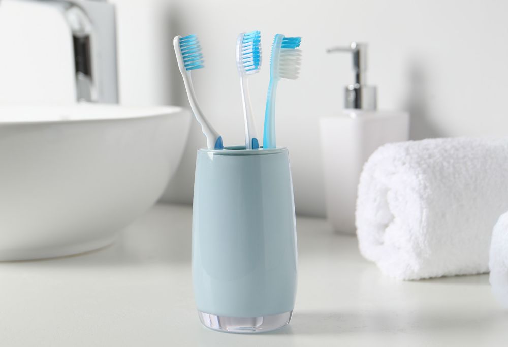 A light blue cup with three toothbrushes inside of it sits by sink. 