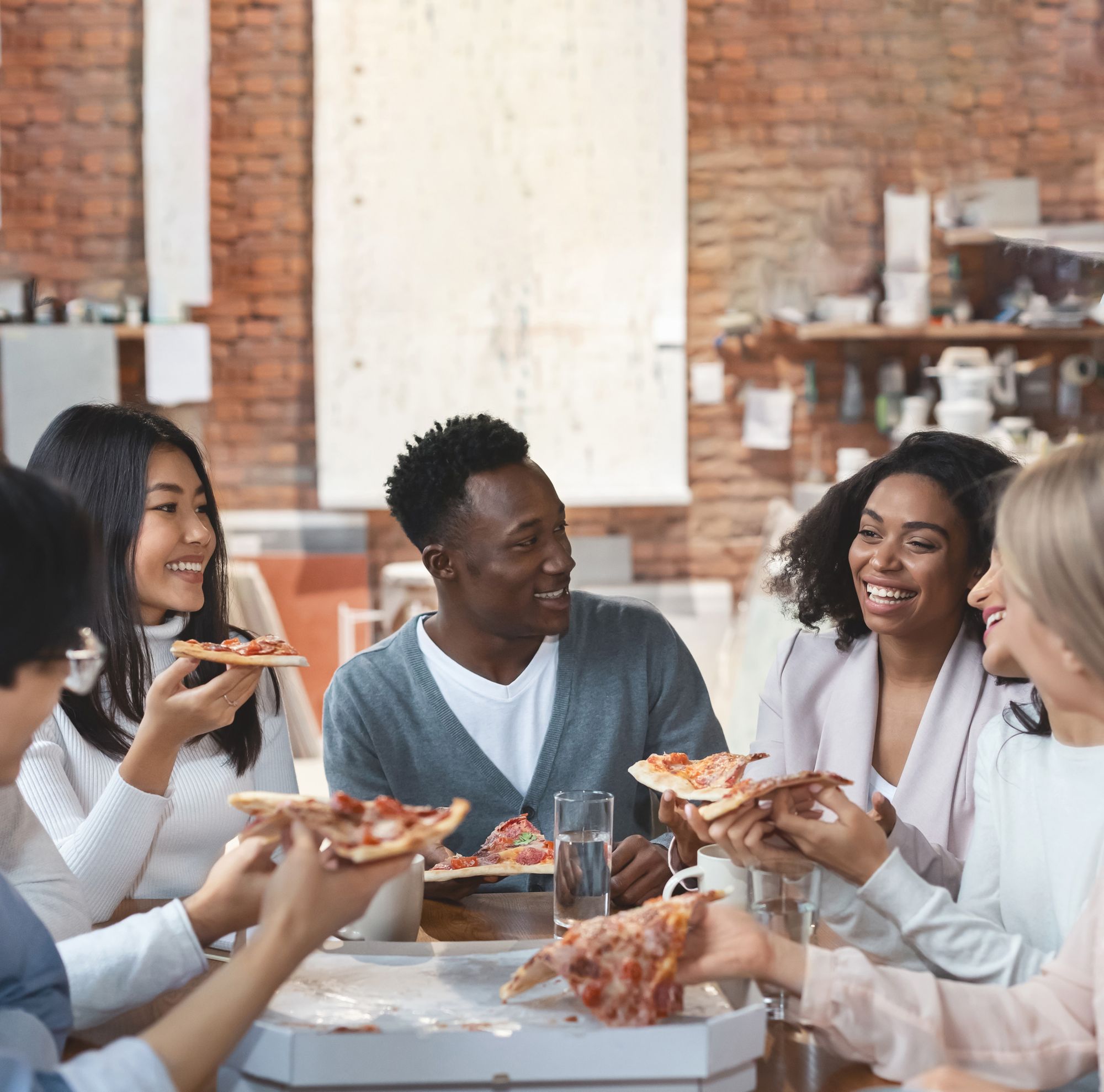 Five interns sitting around a table smile as they each hold a slice of pizza. 