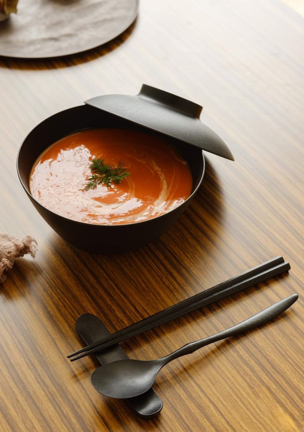 Soup served in a black, heat-resistant bowl with chopsticks and a spoon. 