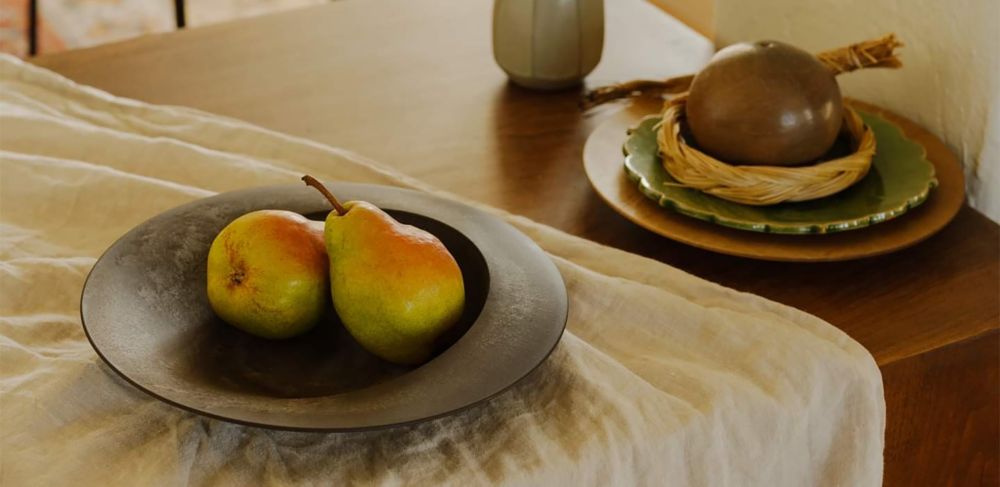 Two yellow-green pears sitting in a dark, earth-tone colored bowl. 