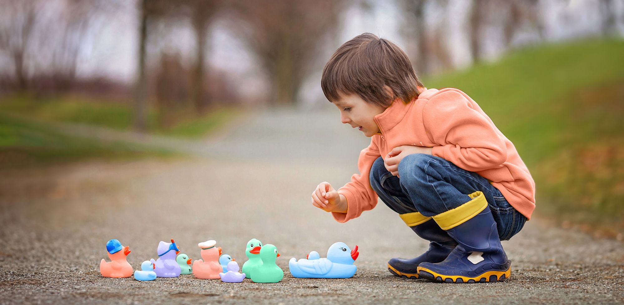 A child lines rubber ducks up in a row on the ground. 