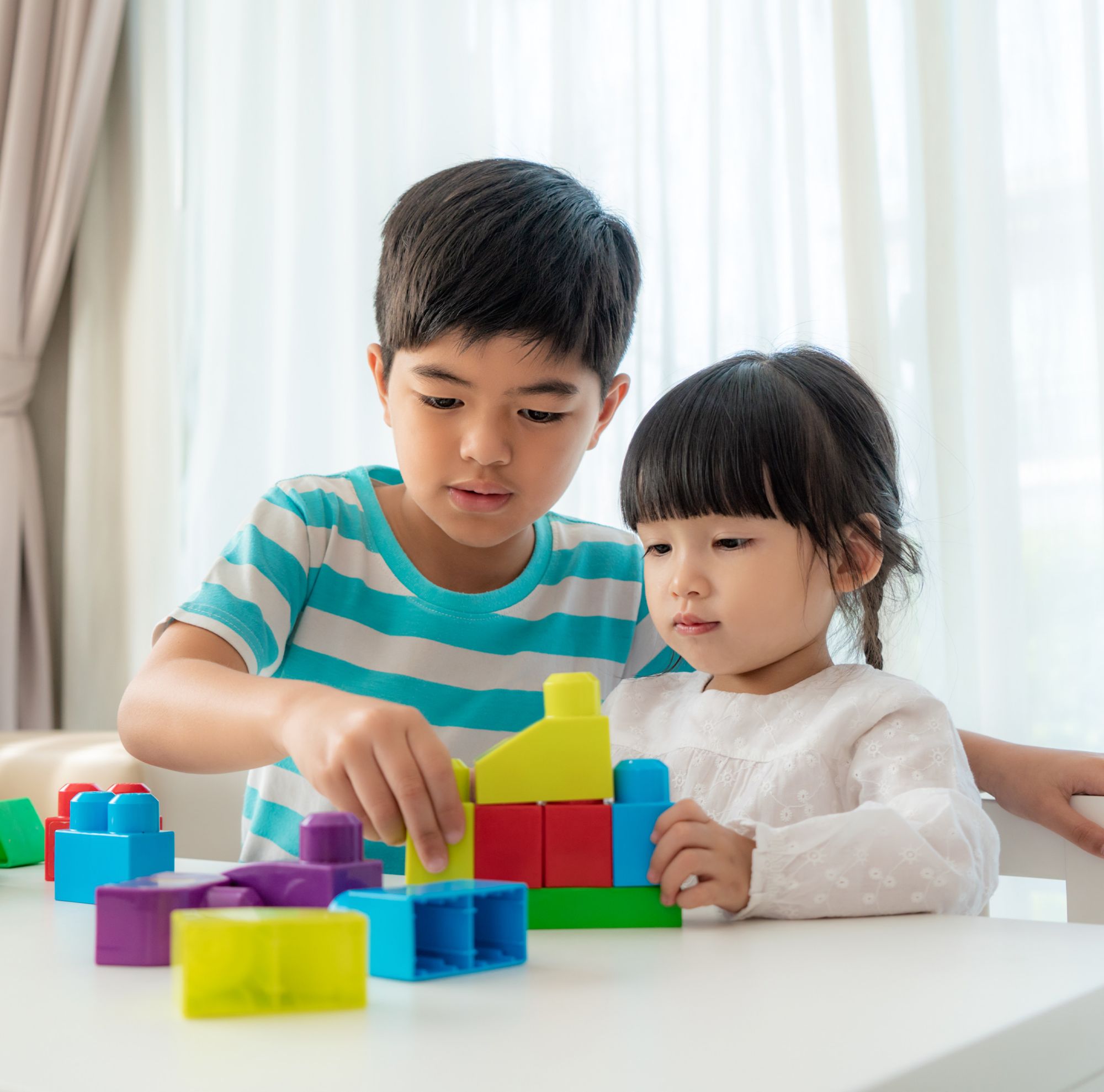 Two kids are building a colorful structure with plastic blocks. 
