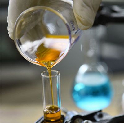 A lab technician pours orange liquid from a beaker to a test tube.  