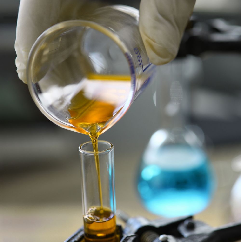 A lab technician pours orange liquid from a beaker to a test tube. 