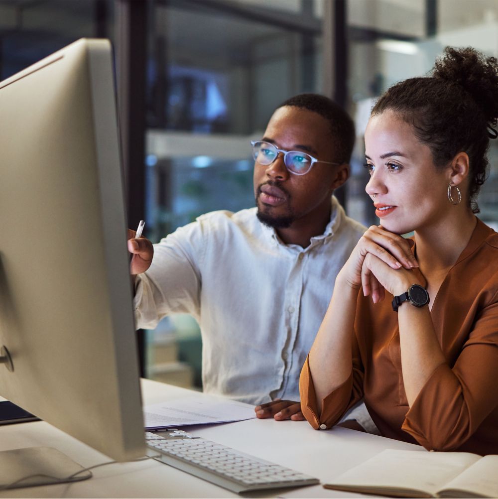 Two employees looking at a desktop computer.   