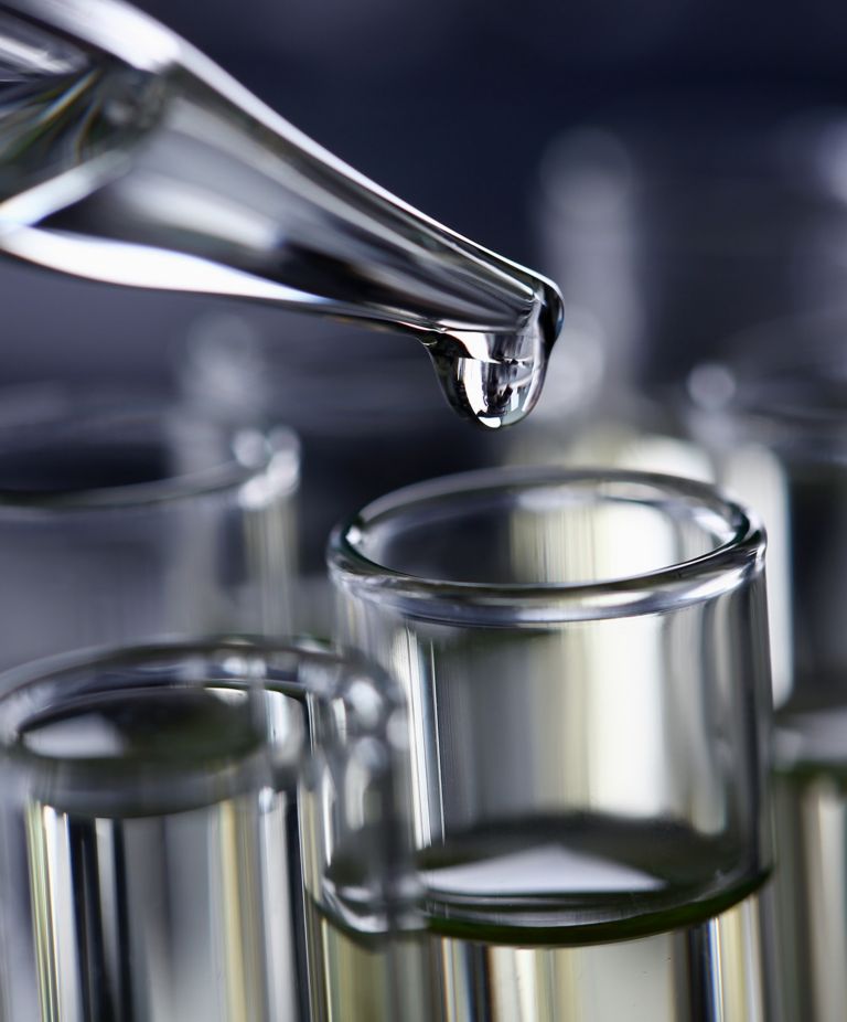 Liquid drips from a dropper into a vial surrounded by full vials 