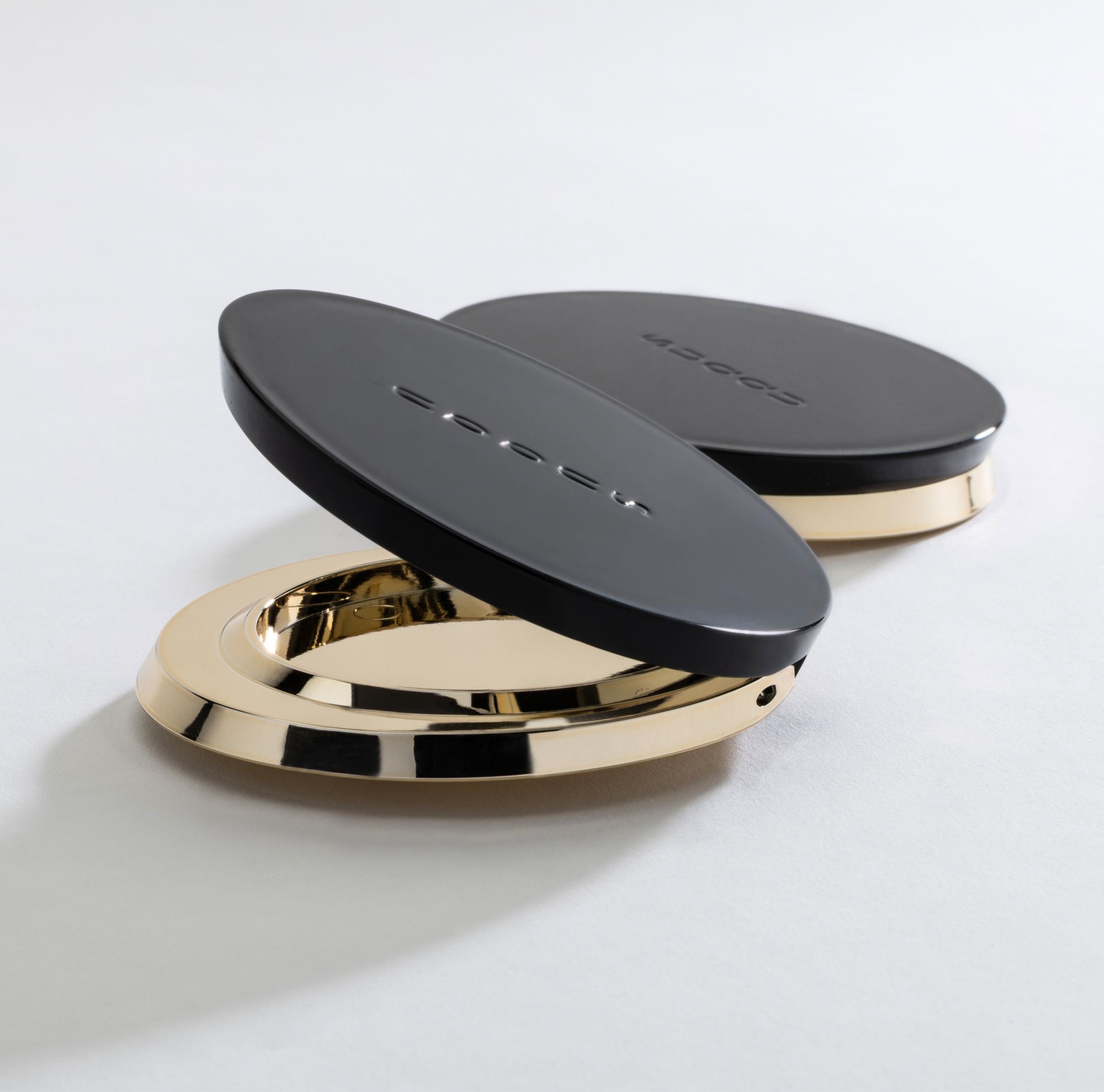 Two metal compacts with a black lid made from Eastman cosmetic packaging material. 