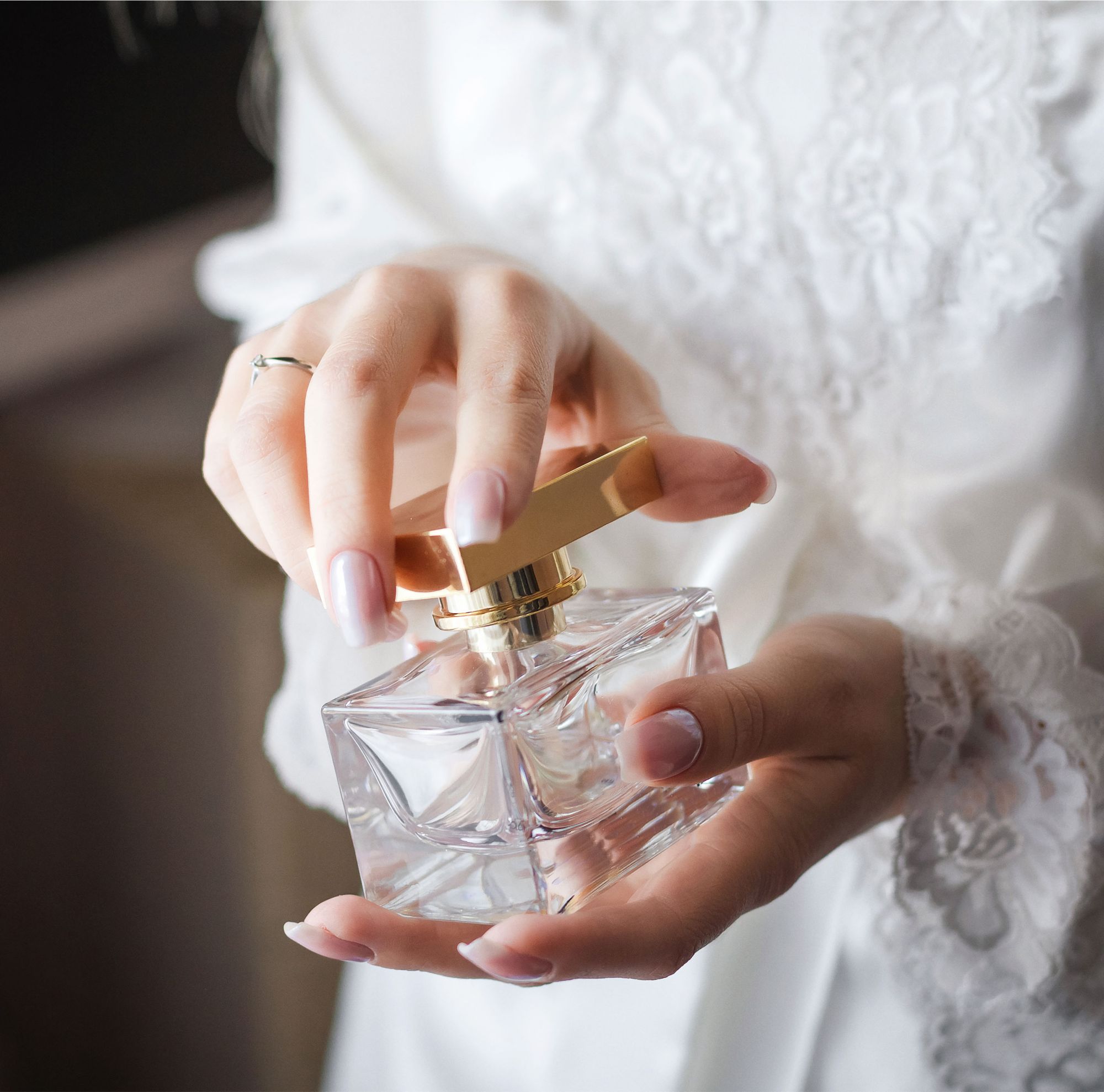 Hands hold a clear bottle of perfume with a gold nozzle.   
