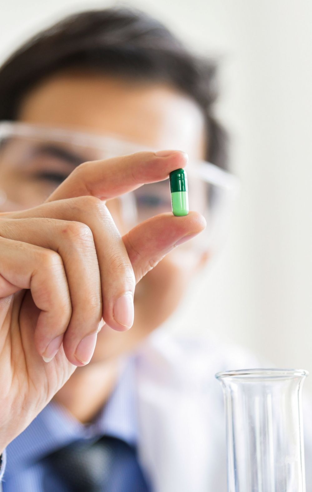 A scientist holding up a two-tone green pill. 