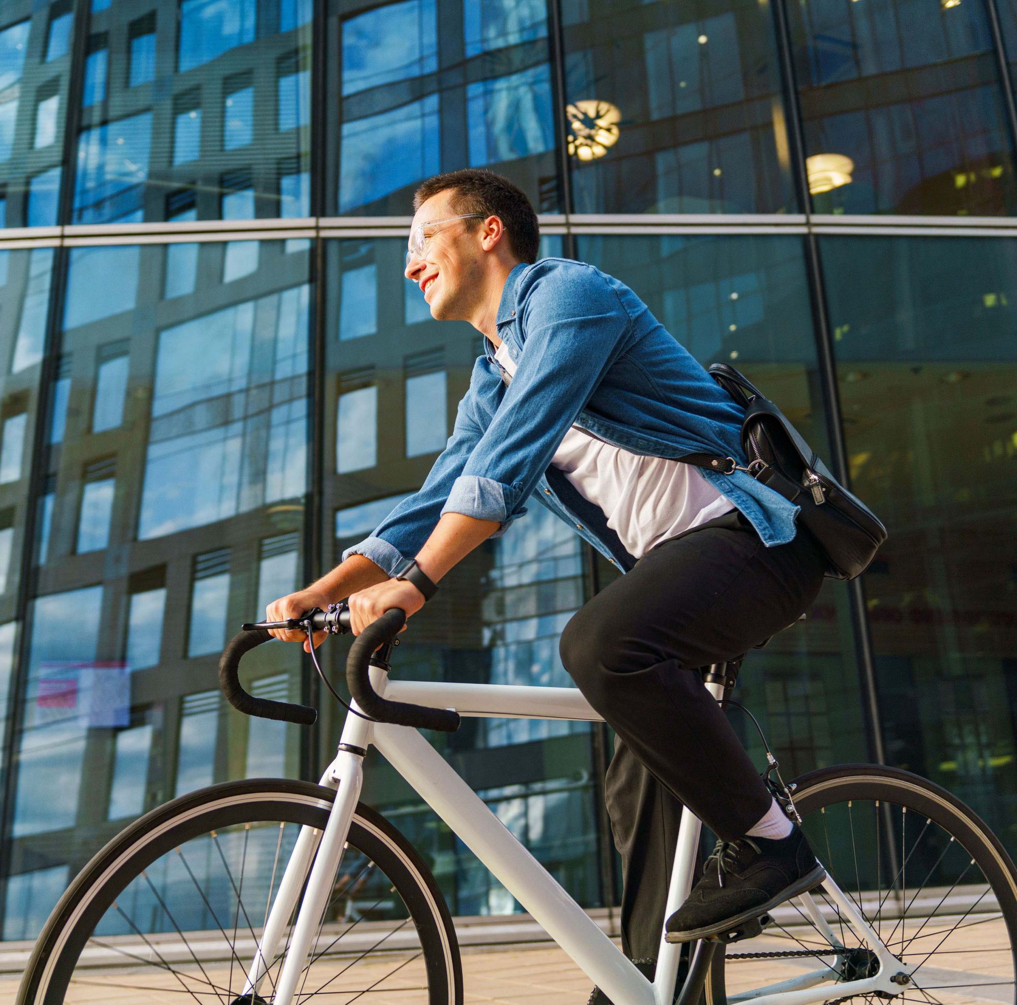 A man with glasses cycling through the city. 