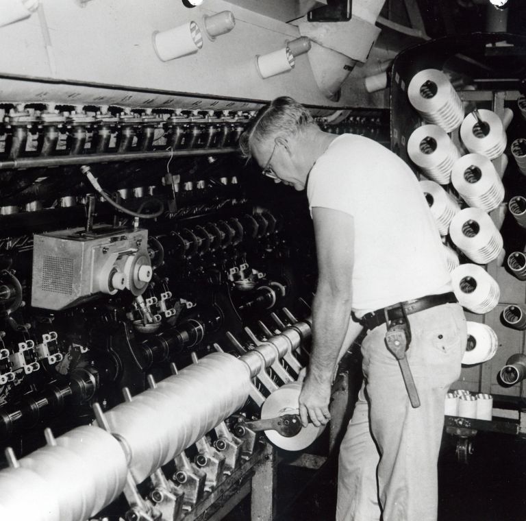 A man operating a textile machine and holding spun fibers. 