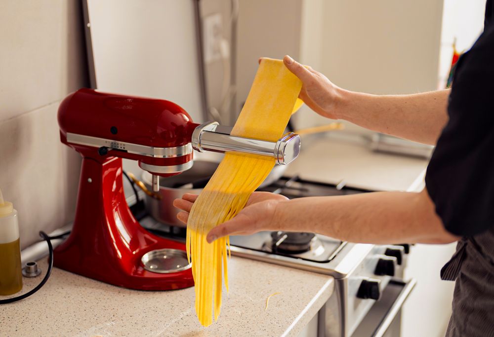 A person uses a red stand mixer to make pasta. 