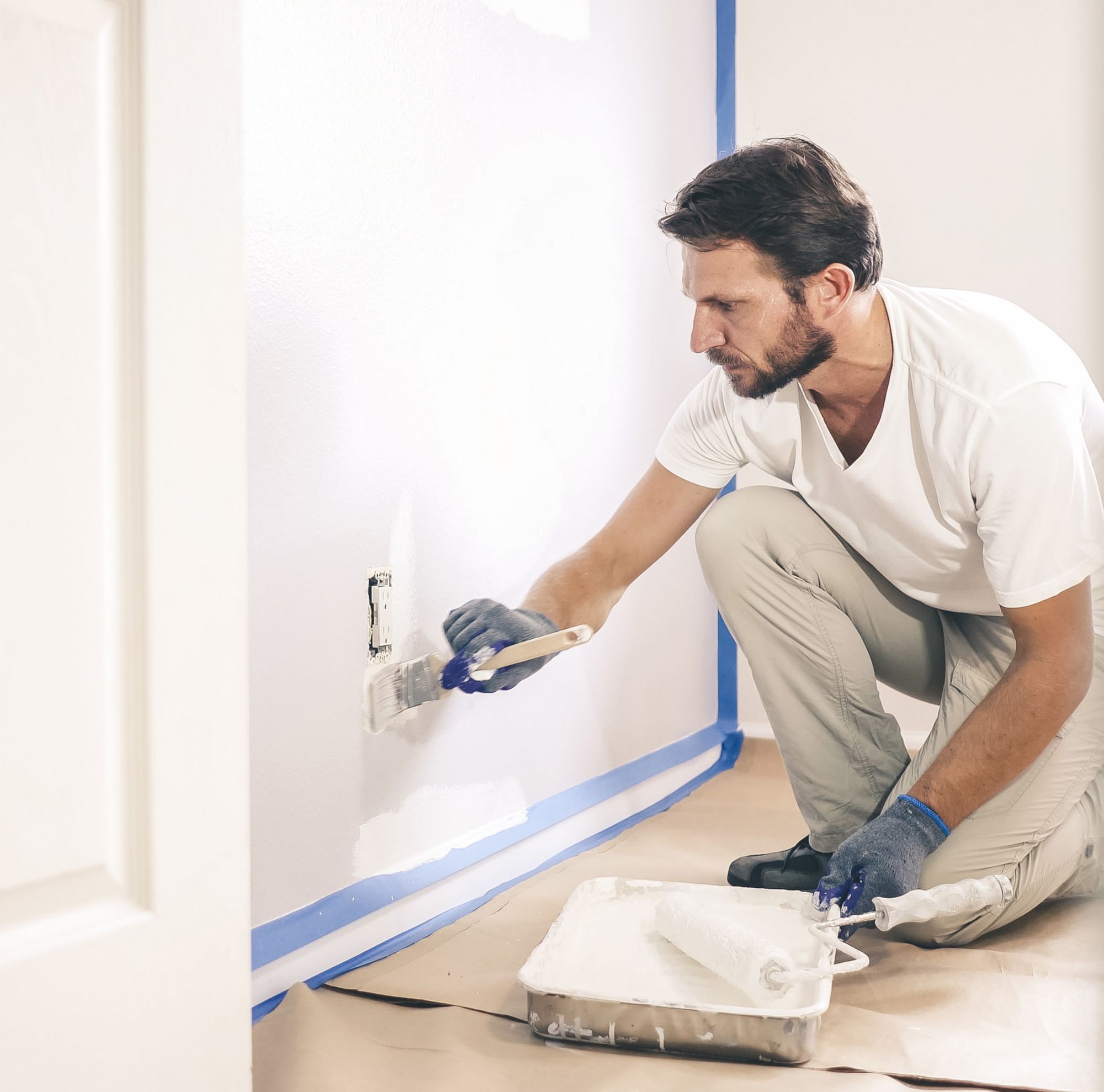 A man kneels while painting a wall. 