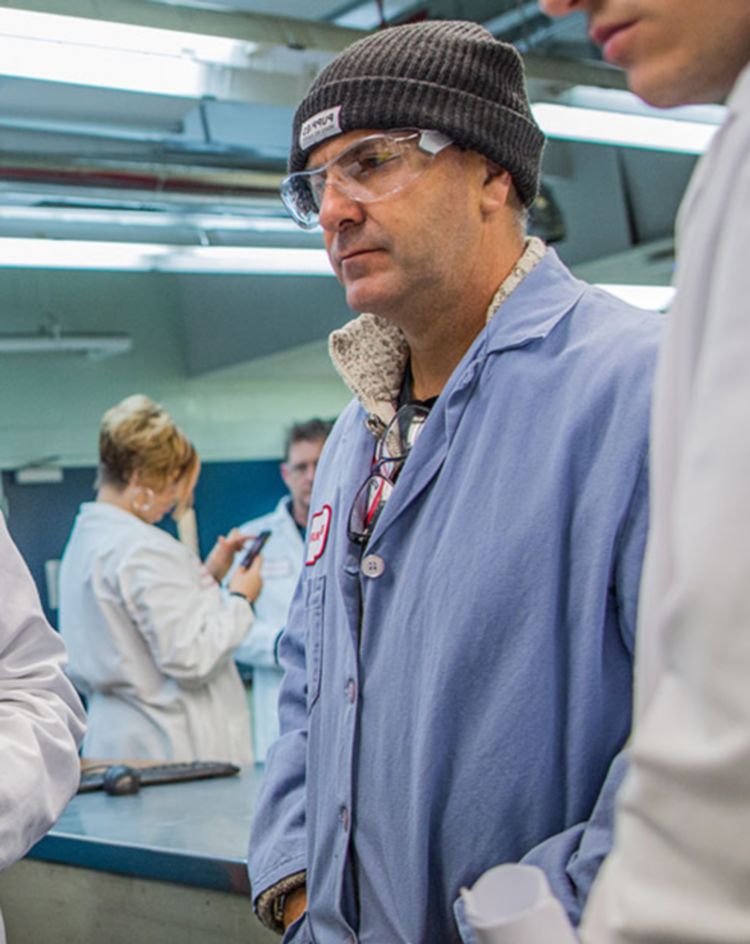 People in lab coats standing together in a manufacturing or laboratory workspace. 