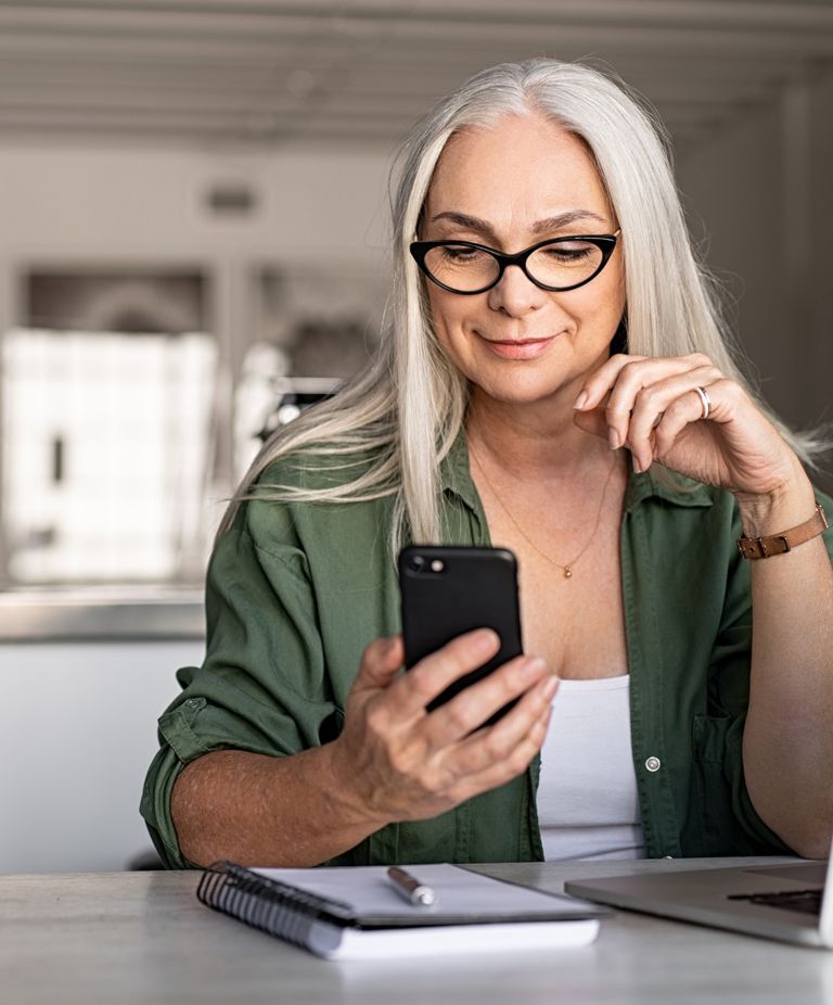 A person with glasses sitting at a table using her phone. 