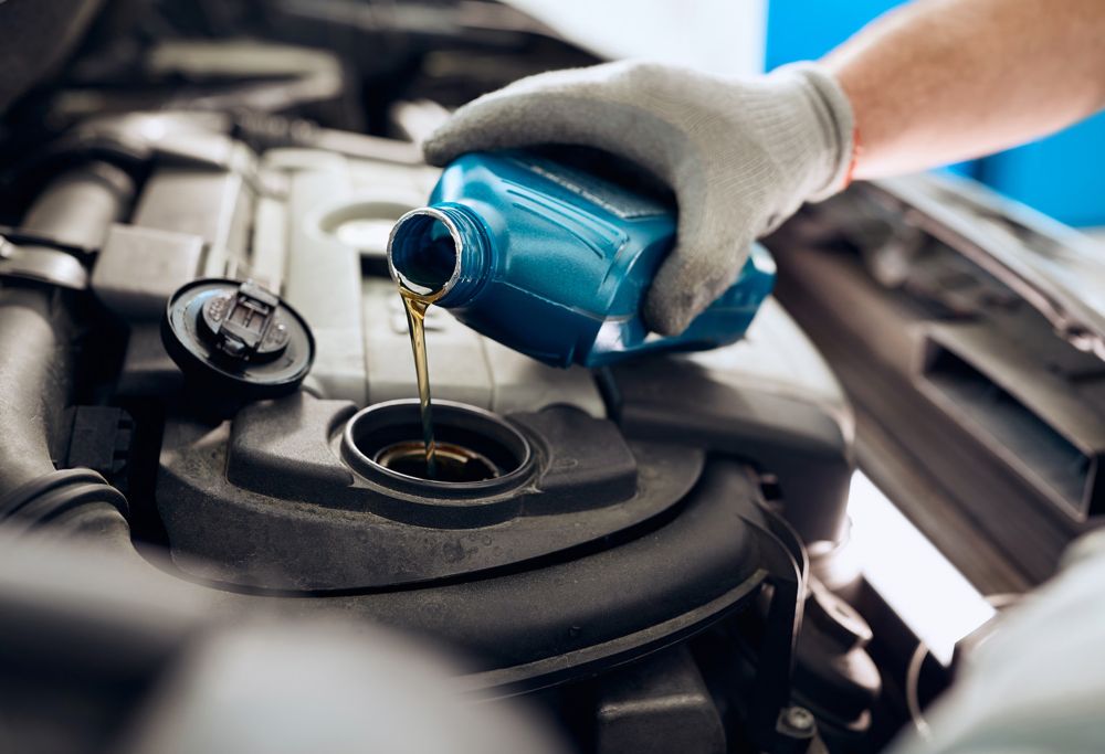 A person pours oil from a bottle into an engine. 