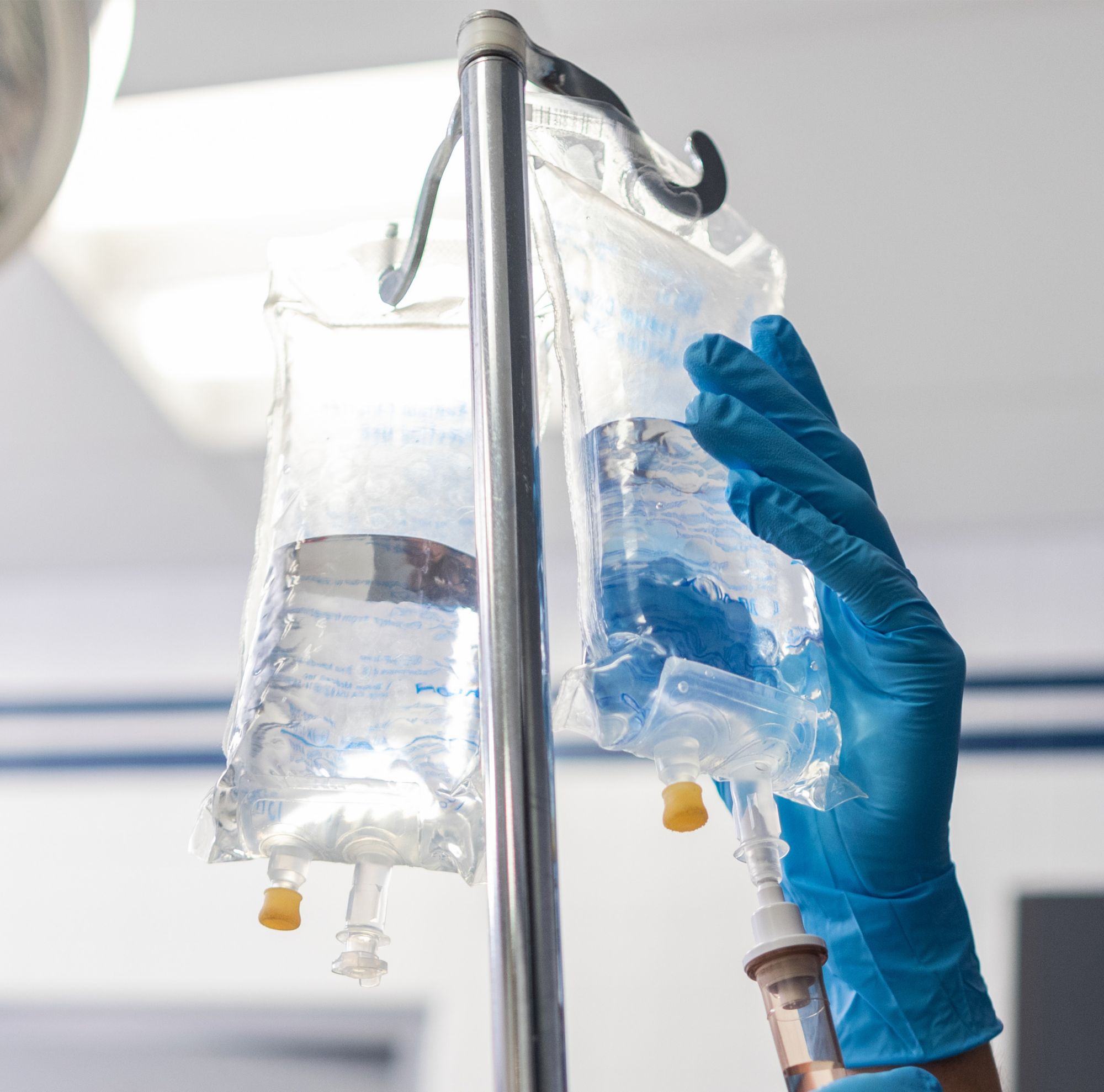 Gloved hand holding a hanging IV bag.   