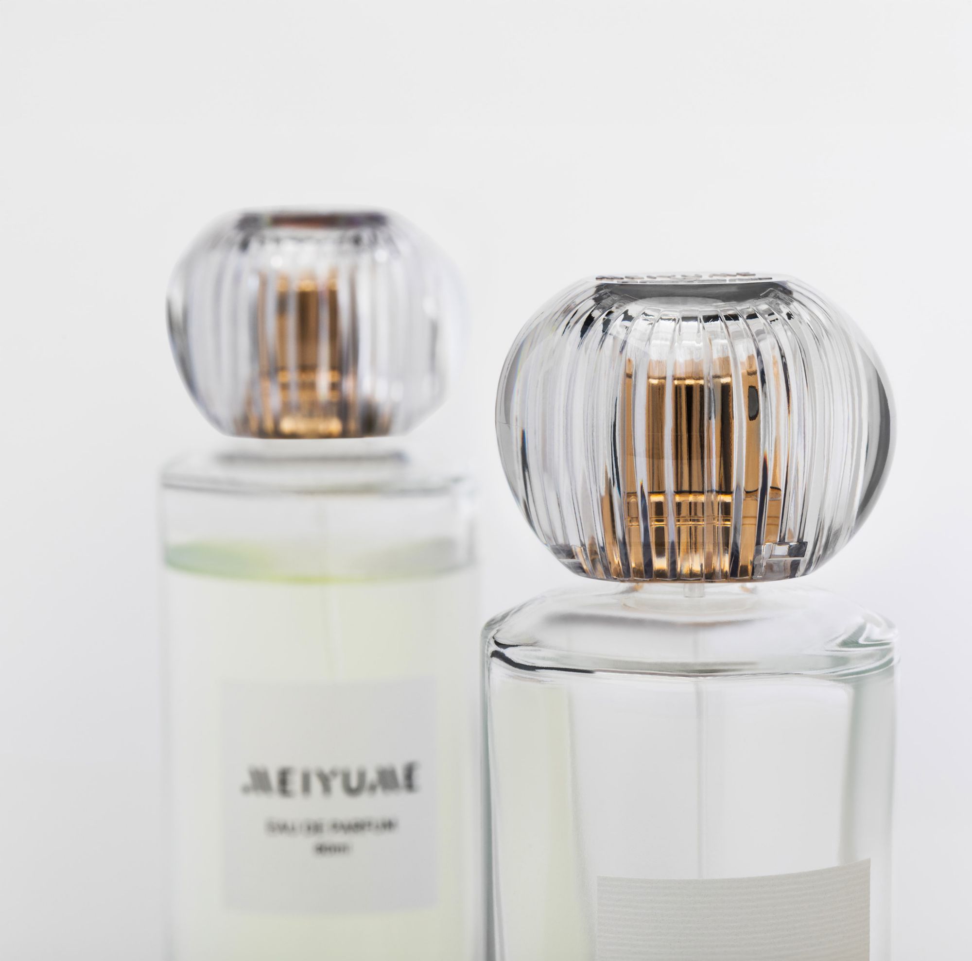 Close-up of two perfume bottles featuring the Meiyume fragrance cap with a clear, ribbed design and gold interior accents. 