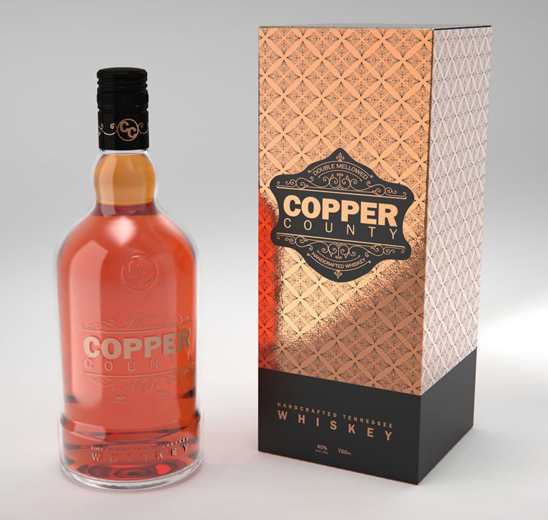 A Copper County whiskey bottle is displayed beside its paper box, featuring a matte black and shiny gold design. 