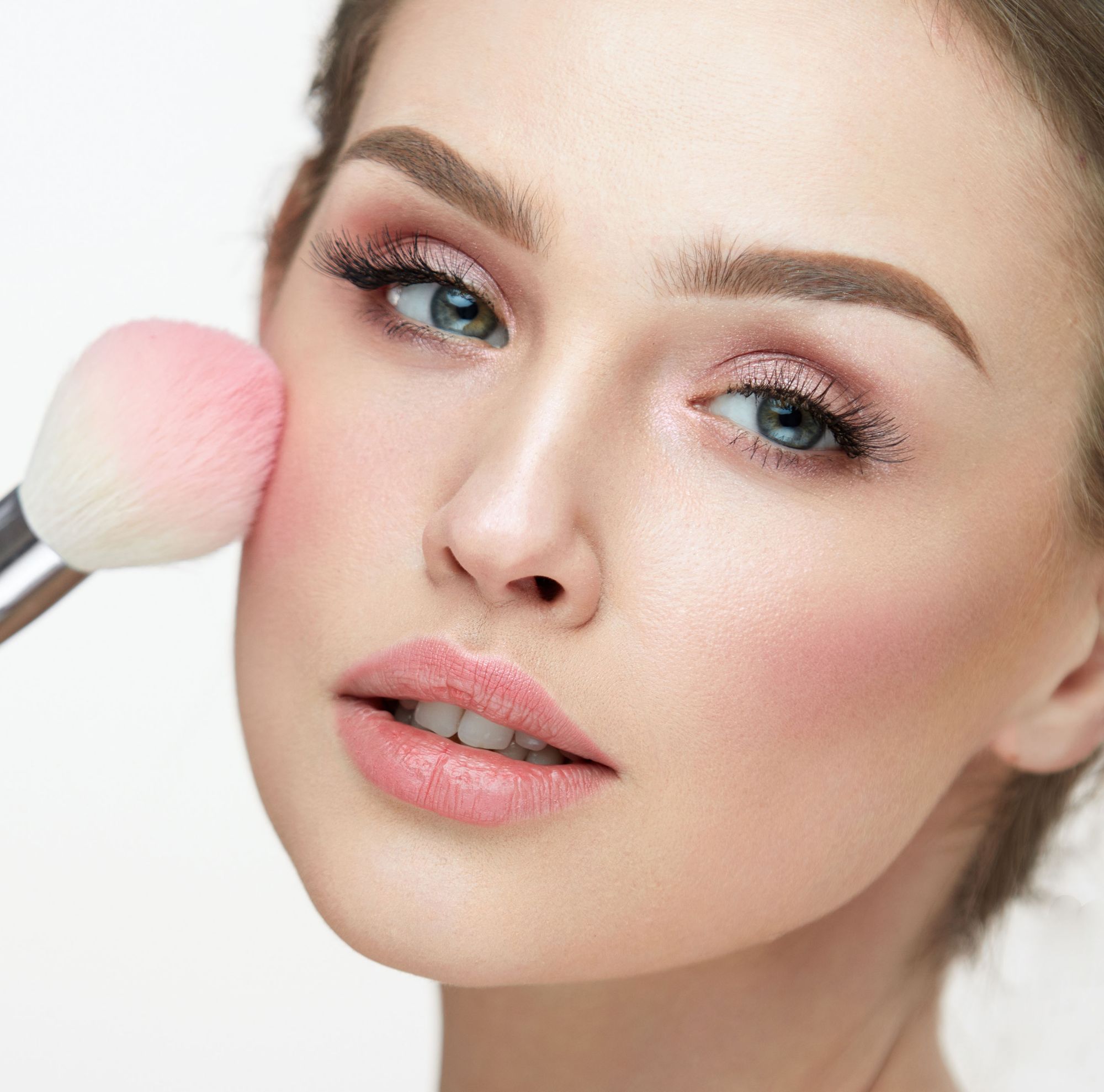 A person applies pink blush with a makeup brush. 